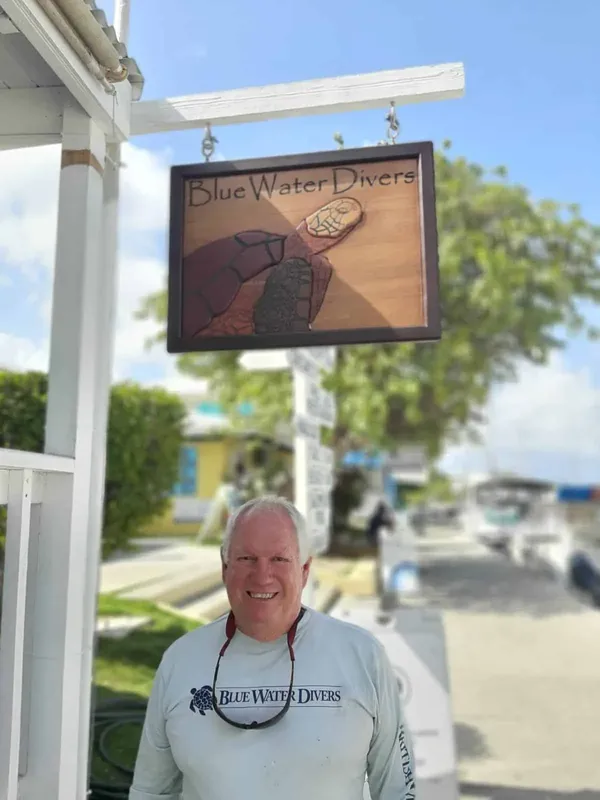 Homme souriant devant l'enseigne d'un centre de plongée ensoleillé