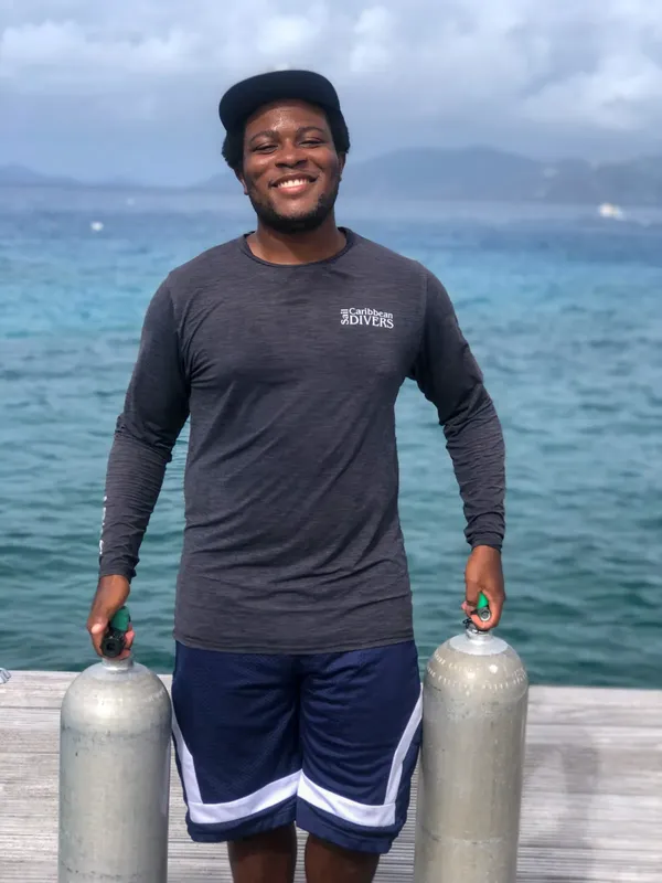 Un homme souriant tient deux bouteilles de plongée sur un ponton