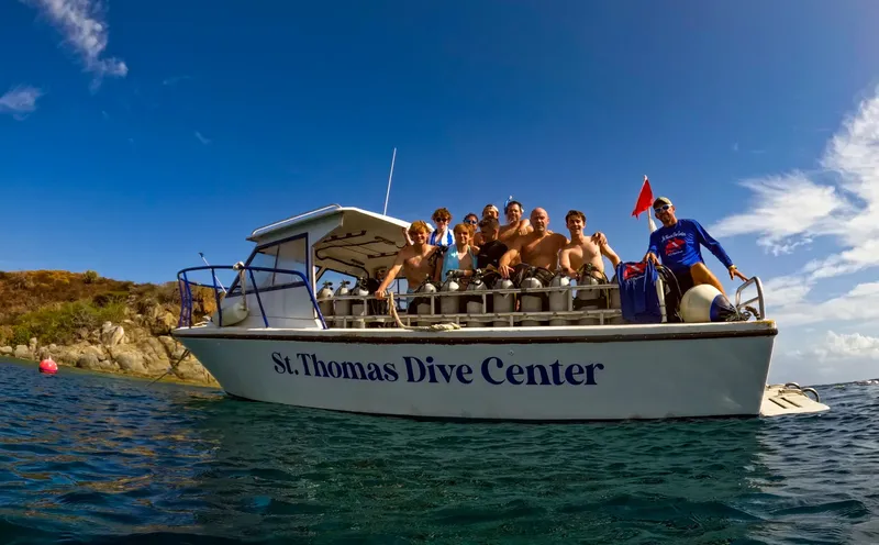 Groupe de plongeurs souriants sur un bateau en mer, ciel bleu