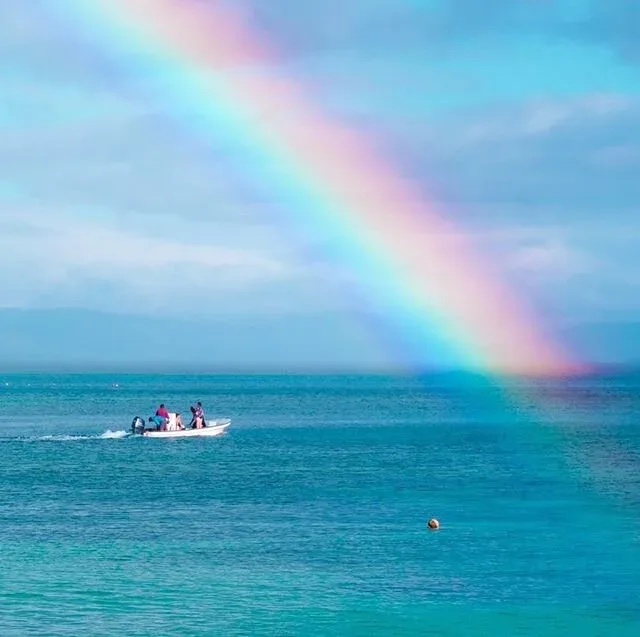 Petit bateau navigue sur une mer calme sous un arc-en-ciel