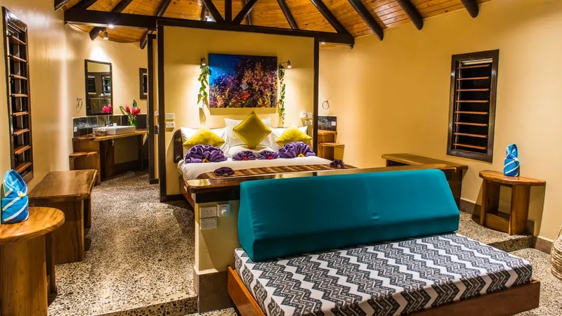 Chambre d'hôtel tropicale avec lit décoré et coin salon confortable