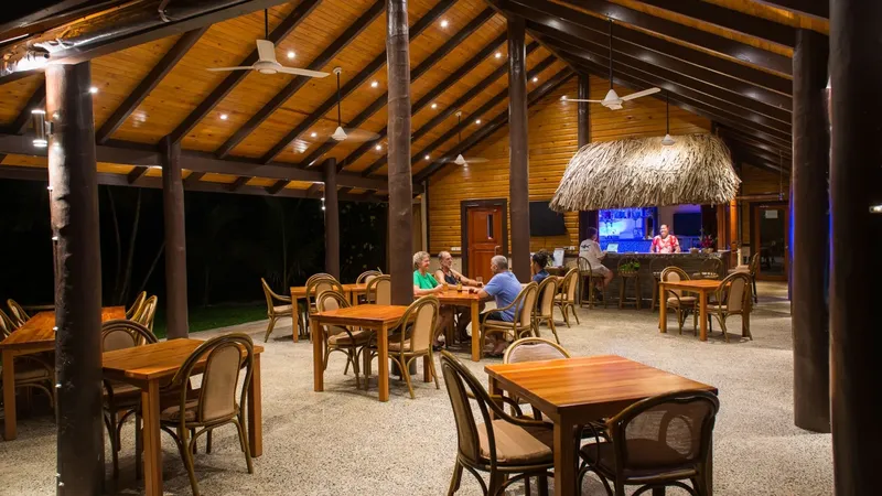 Terrasse ouverte avec tables, chaises et personnes assises, éclairage nocturne