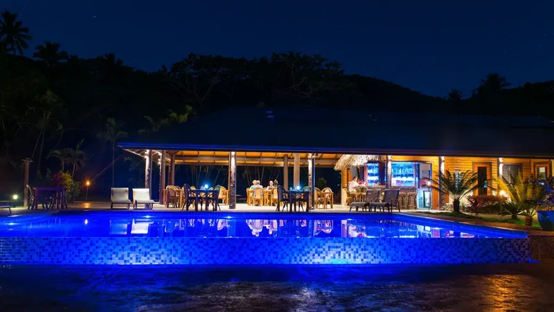 Bâtiment éclairé avec piscine bleue et personnes assises à table