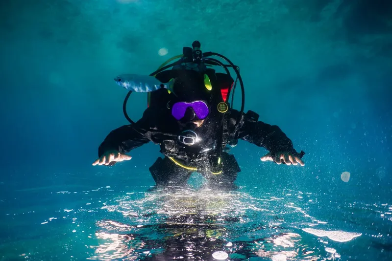 Plongeur en combinaison noire nageant vers la caméra dans l'eau bleue