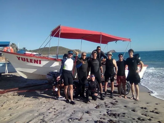 Groupe de plongeurs souriants posant devant un bateau sur la plage