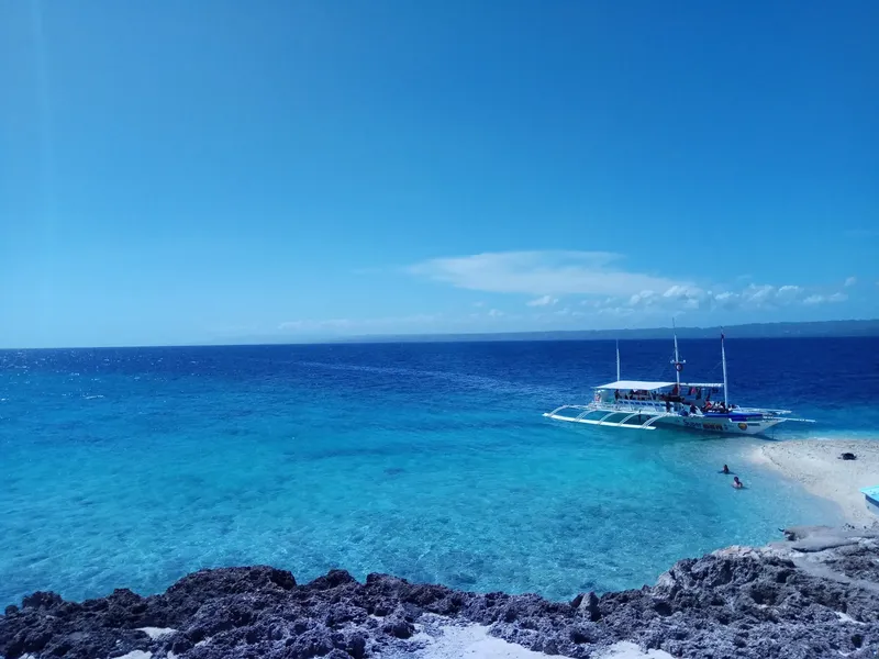 Bateau de plongée amarré dans une crique turquoise avec des baigneurs