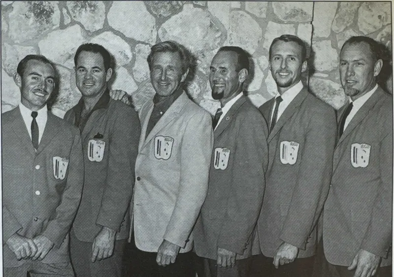 Six hommes souriants en costume posent devant un mur en pierre