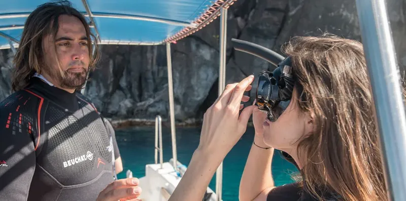 Un moniteur ajuste le masque d'une plongeuse sur un bateau