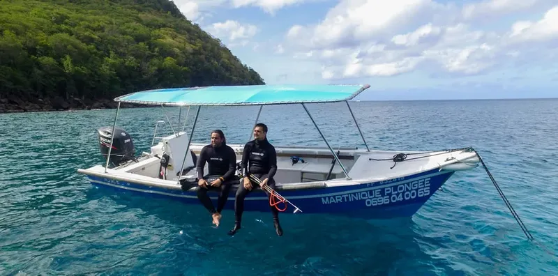 Deux plongeurs assis dans un bateau blanc sur mer turquoise