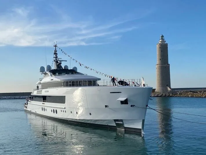 Grand yacht amarré dans un port avec un phare en arrière-plan