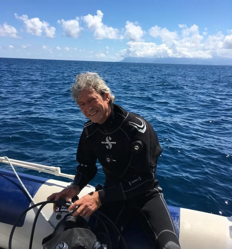 Plongeur souriant assis sur un bateau en mer, combinaison noire
