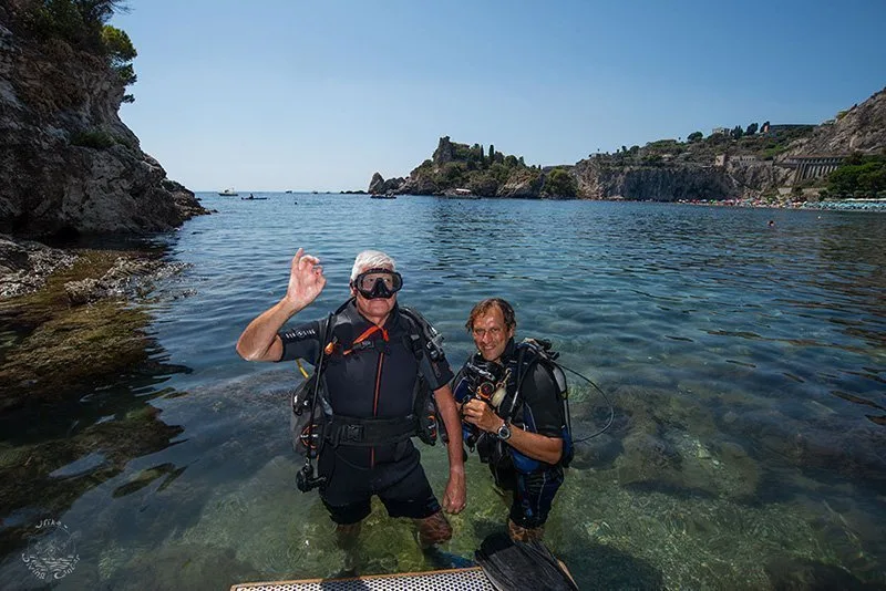 Deux plongeurs souriants dans l'eau peu profonde près d'une côte rocheuse