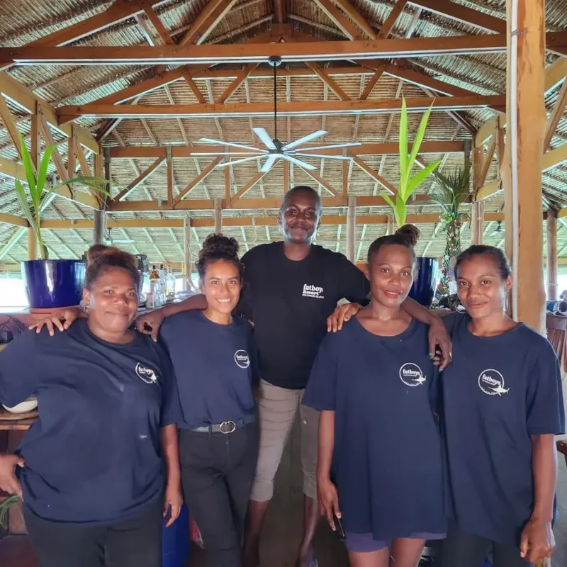 Cinq personnes souriantes posent sous une structure en bois et palmes