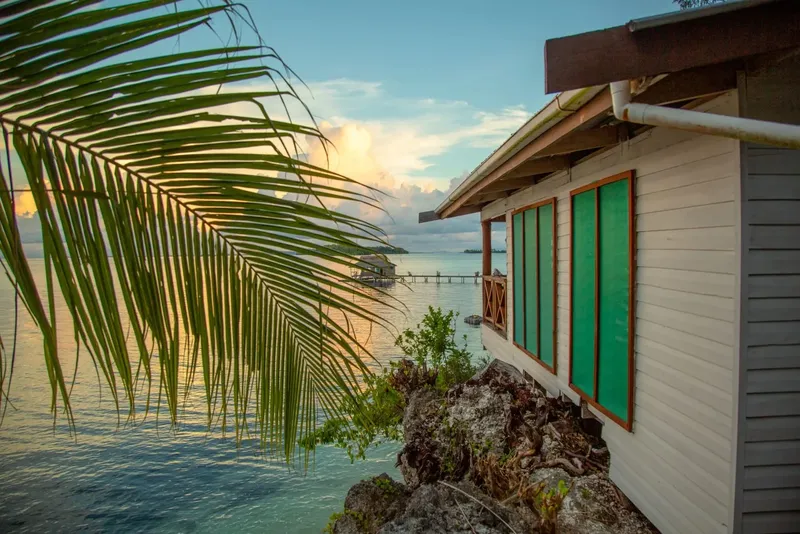 Bâtiment blanc au bord de l'eau avec palmiers et coucher de soleil