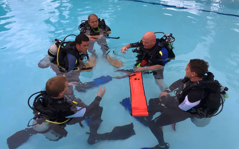 Quatre plongeurs en formation discutent dans une piscine claire