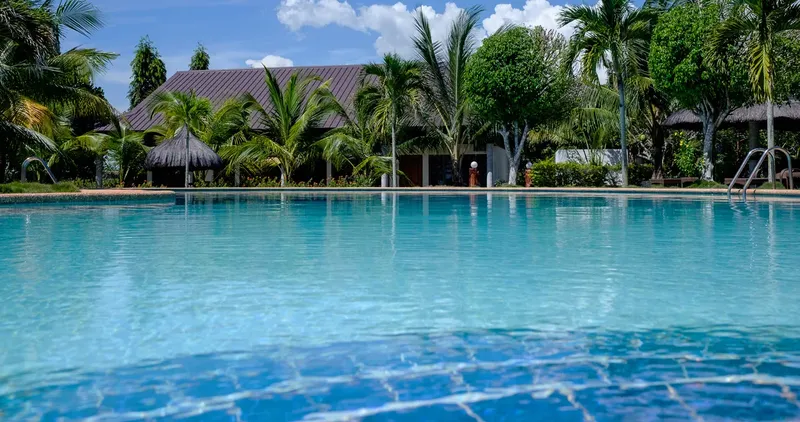 Piscine turquoise devant un bâtiment avec végétation tropicale et ciel bleu