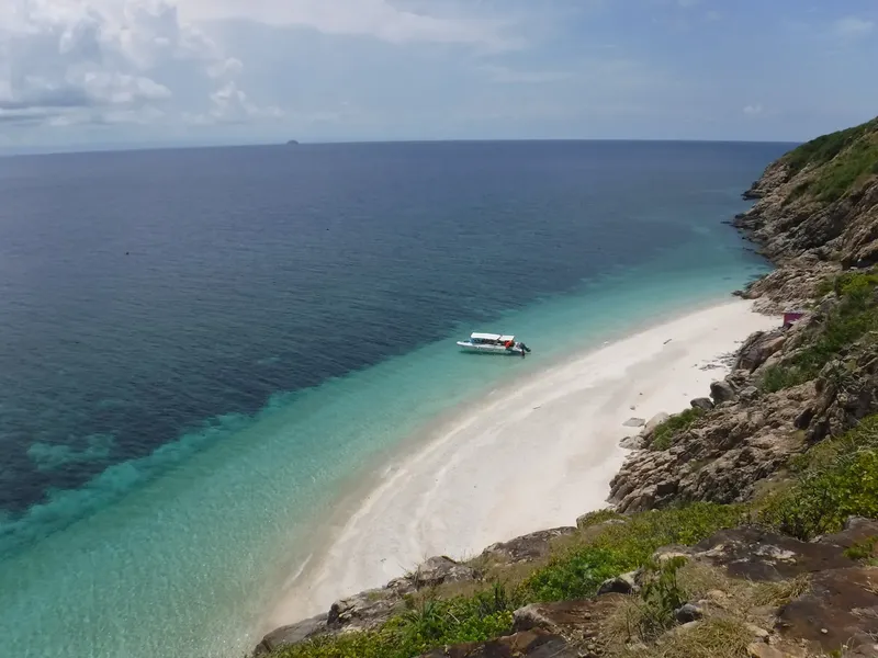 Plage de sable blanc, mer turquoise et bateau en mer