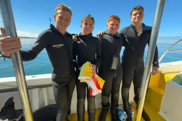 Quatre plongeurs en combinaison sur un bateau, souriants et détendus