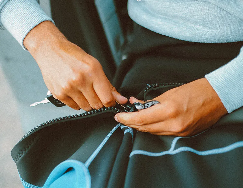 Mains fermant une combinaison de plongée noire avec un zip bleu