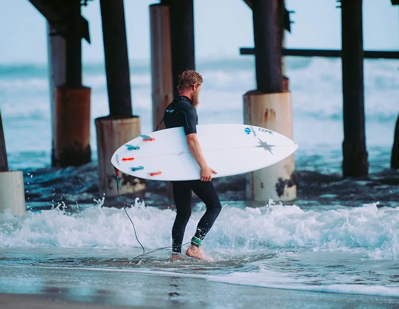 Un surfeur sort de l'eau avec sa planche sous un ponton