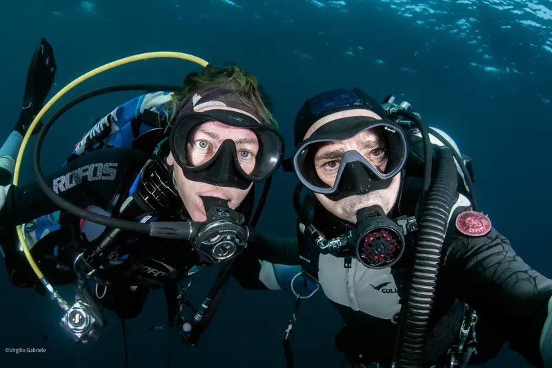 Deux plongeurs souriants, équipés, flottent face à la caméra sous-marine