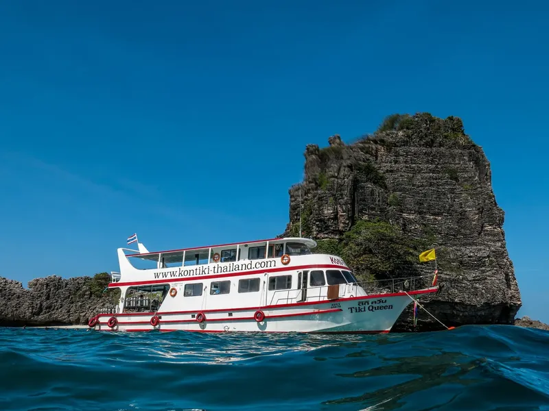 Bateau de plongée blanc et rouge au large d'une île rocheuse