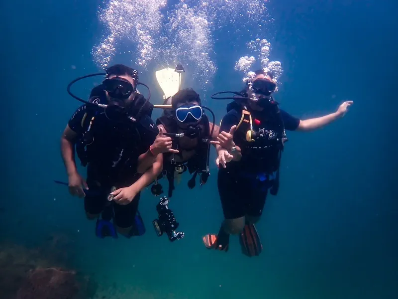 Trois plongeurs souriants nagent ensemble dans une eau bleu clair