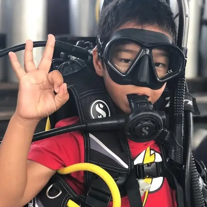 Jeune plongeur souriant, équipé, faisant un signe de la main