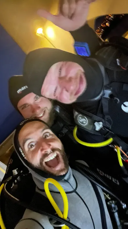 Quatre plongeurs souriants en équipement complet, posant pour un selfie