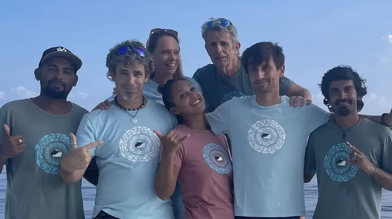 Groupe de six personnes souriantes sur un bateau, geste de la main