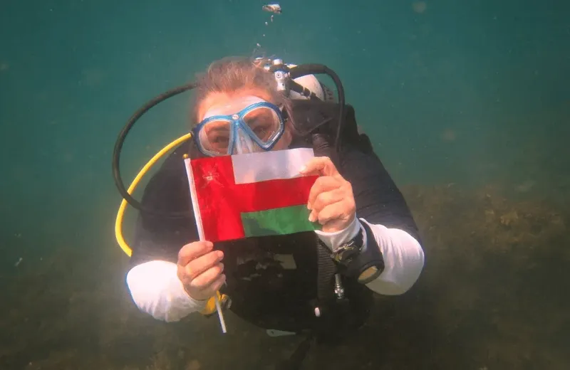 Plongeur souriant tenant un drapeau omanais sous l'eau
