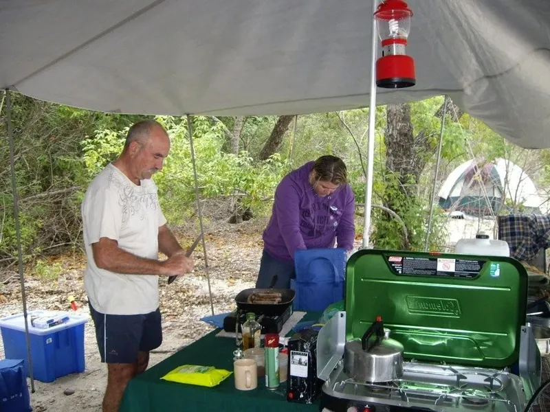 Deux personnes préparent un repas sous un abri de camping extérieur