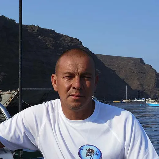 Homme souriant sur un bateau avec la mer et des montagnes