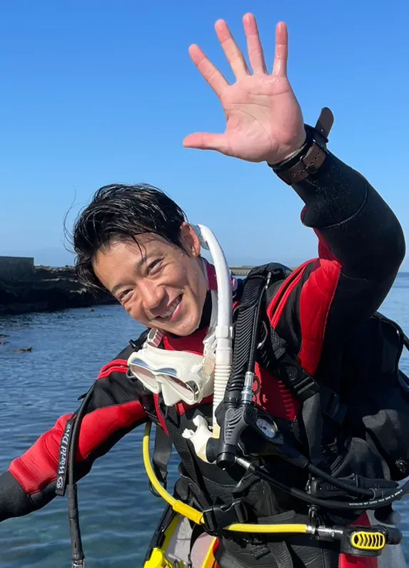 Plongeur souriant salue avec la main, équipé en surface, mer claire