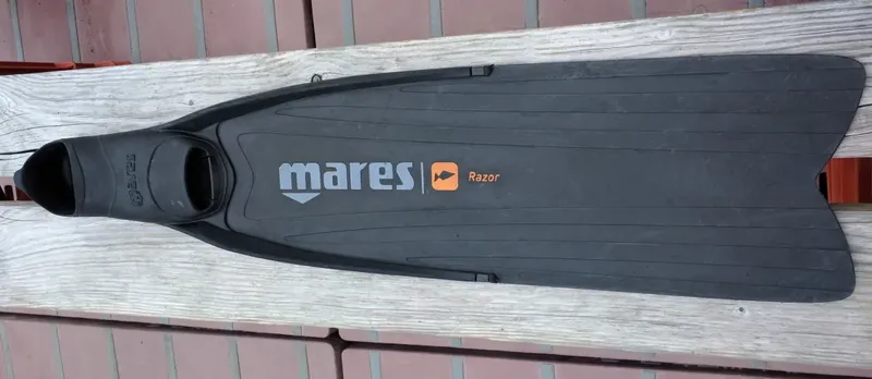 Palme de plongée Mares Razor noire allongée sur une surface boisée