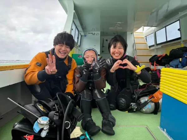 Trois plongeurs souriants à bord d'un bateau, équipés et prêts