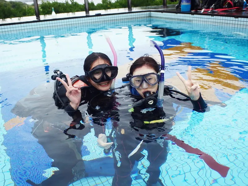 Deux plongeuses souriantes en combinaison dans une piscine avec du matériel