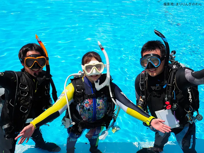 Trois plongeurs équipés sourient dans une eau turquoise claire