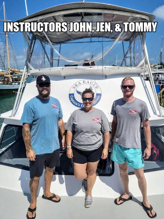 Trois instructeurs de plongée souriants posent devant un bateau blanc