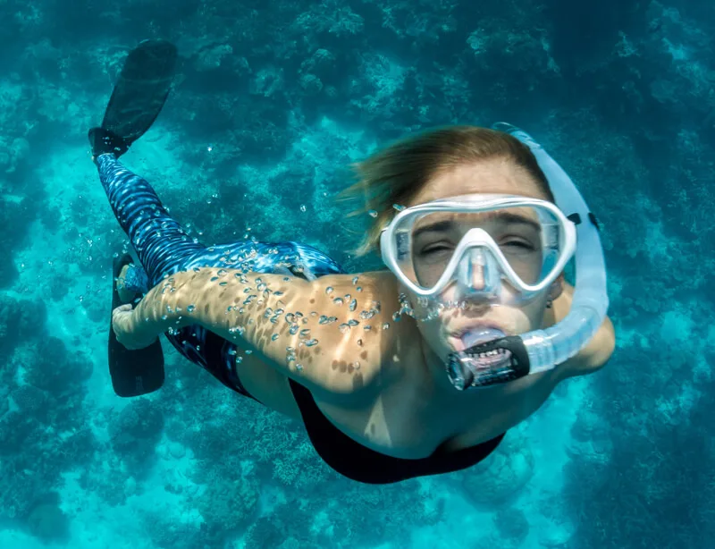 Jeune femme nageant avec masque et tuba dans une eau turquoise