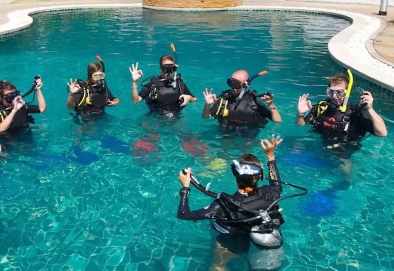 Groupe de plongeurs en formation dans une piscine, sourires et signes