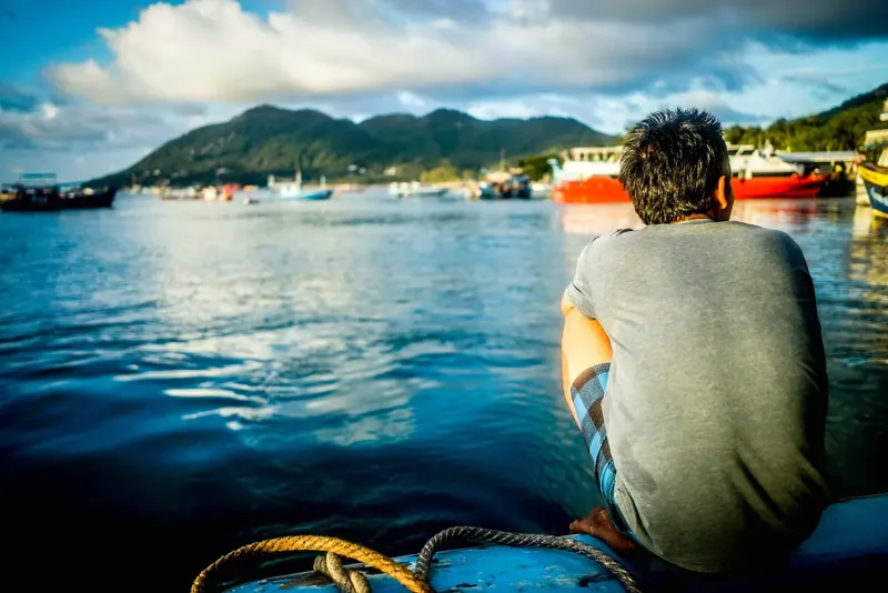 Homme assis sur un bateau regardant la mer et les montagnes