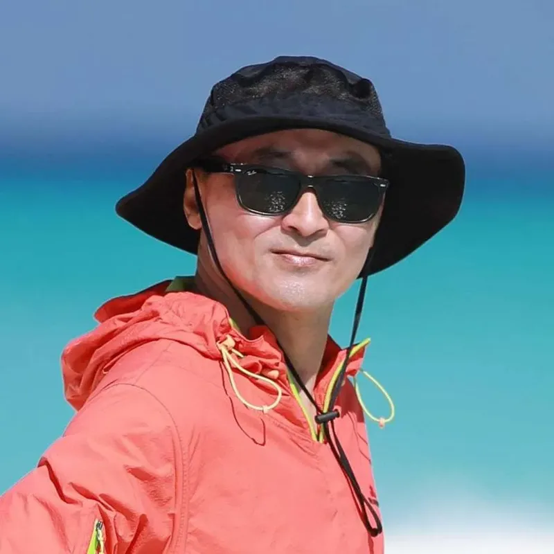 Homme portant un chapeau et des lunettes de soleil devant mer turquoise