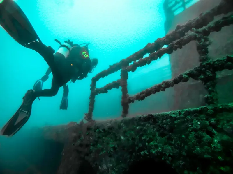 Plongeur explorant une épave métallique sous l'eau, lumière bleutée