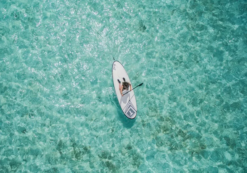Une personne fait du paddleboard sur une eau turquoise et claire