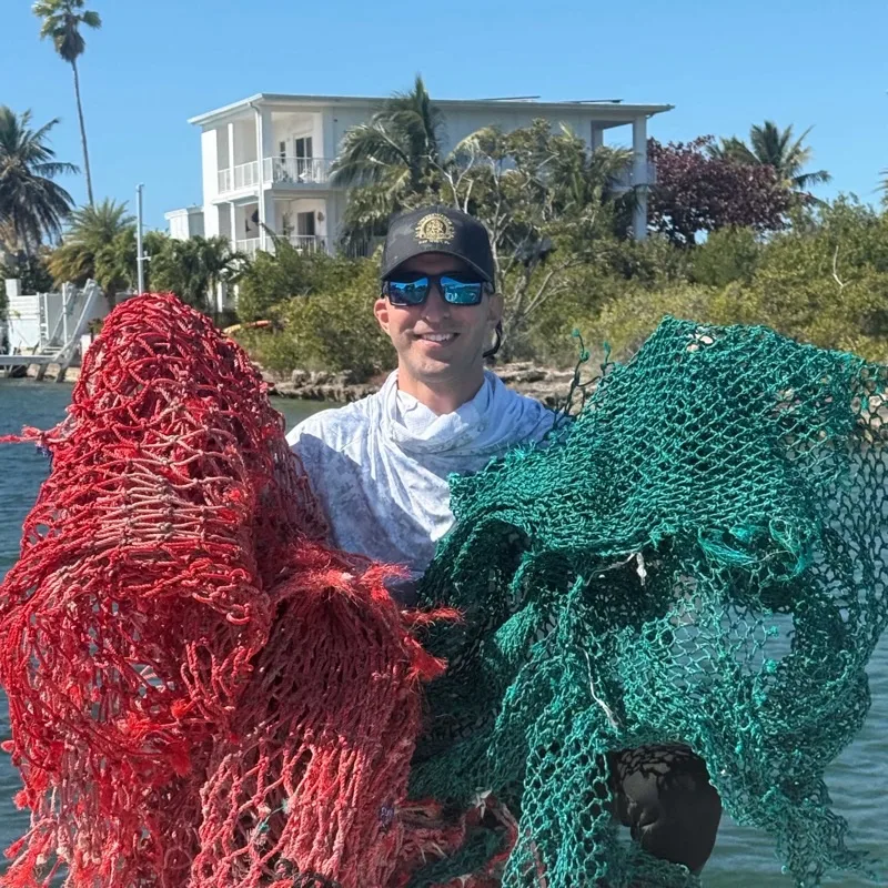 Un homme souriant tient deux filets de pêche colorés en extérieur