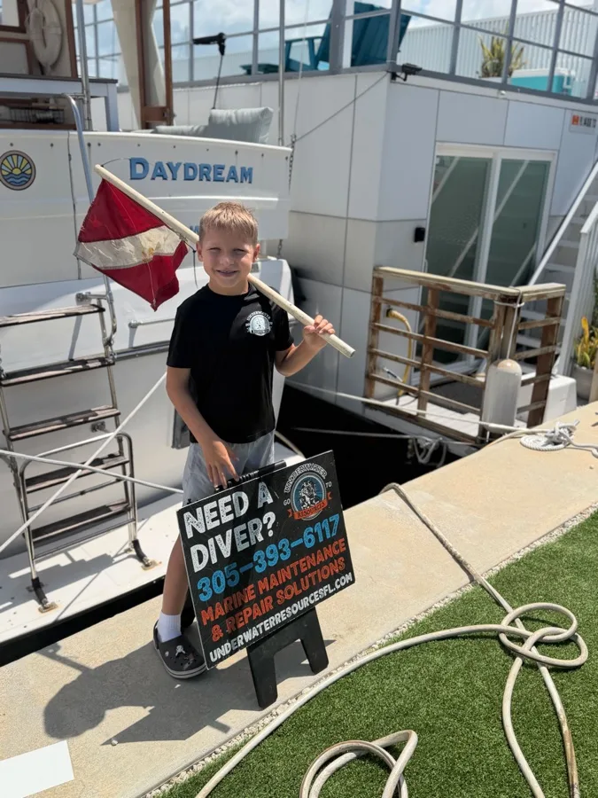 Un enfant tient un drapeau de plongee devant un bateau et une affiche