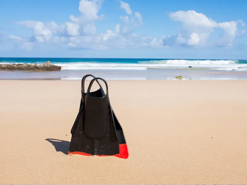 Plaquettes de plongée noires et rouges sur une plage ensoleillée