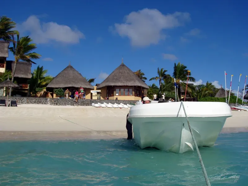 Plage tropicale avec un bateau blanc et des bâtiments à l'arrière-plan