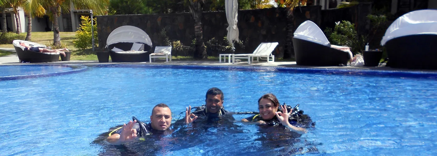 Trois plongeurs souriants dans une piscine, équipés de gilets et masques